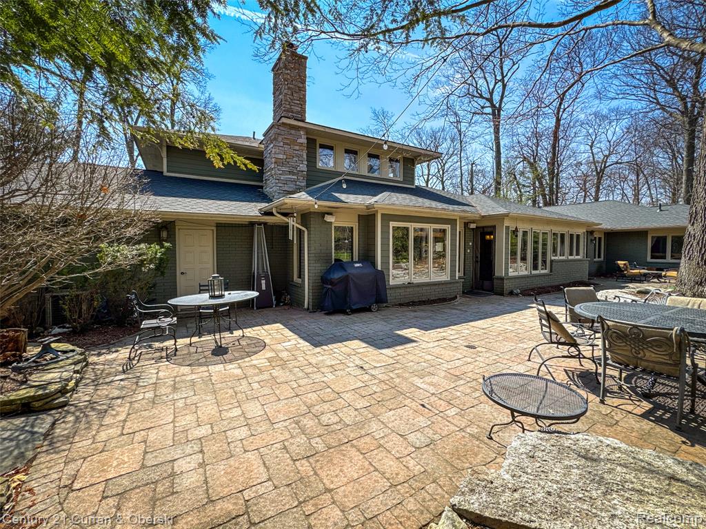 Back of house featuring outdoor dining space, a patio area, a chimney, brick siding, and roof with shingles