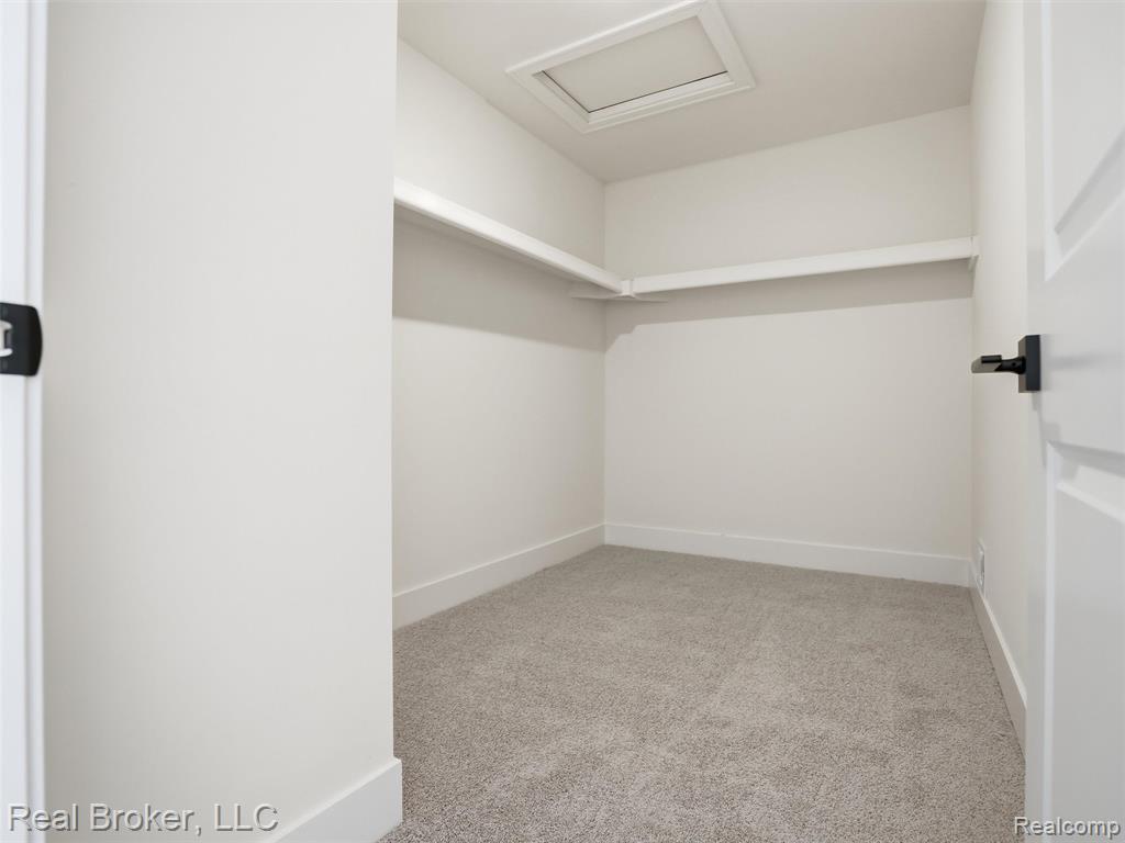 Walk in closet featuring attic access and light colored carpet
