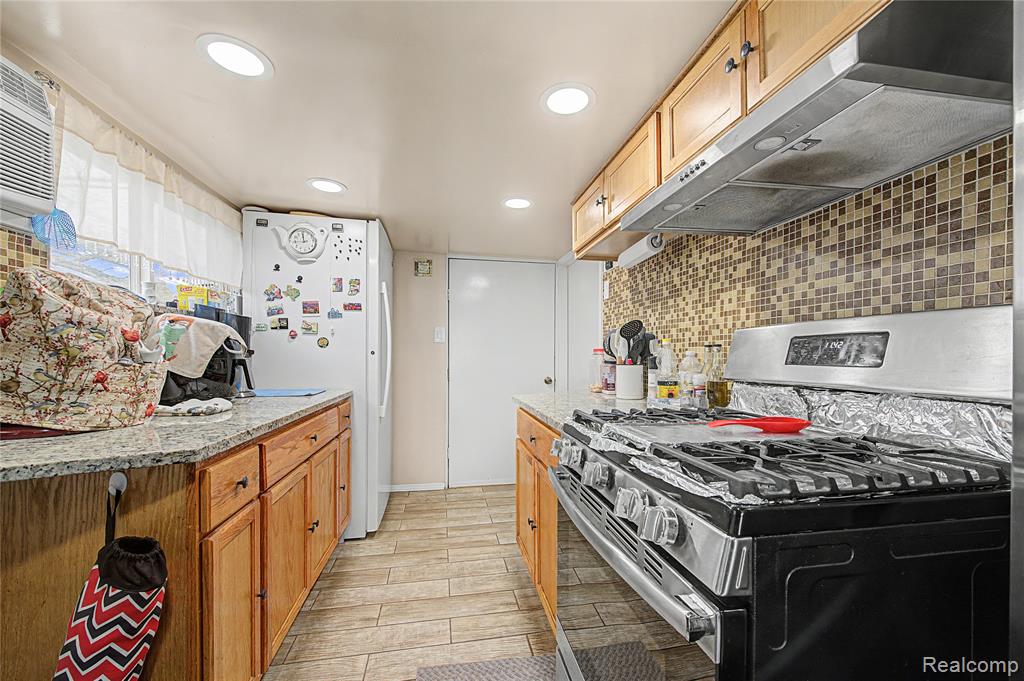 Kitchen with stainless steel gas range oven, freestanding refrigerator, light stone counters, wood tiled floors, and tasteful backsplash