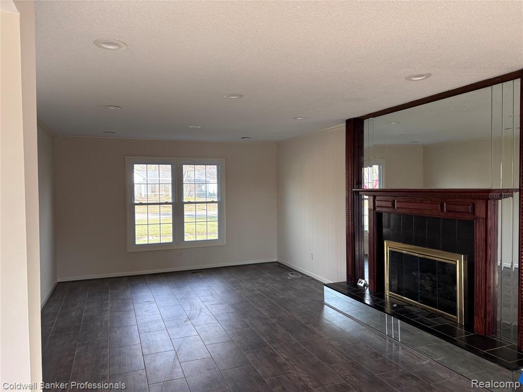 Unfurnished family room with a tiled fireplace, wood tiled floors, and a textured ceiling