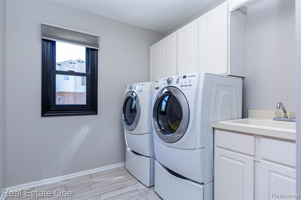 1st floor Laundry area with washing machine and clothes dryer, porcelain tile floors, laundry tub and storage cabinets