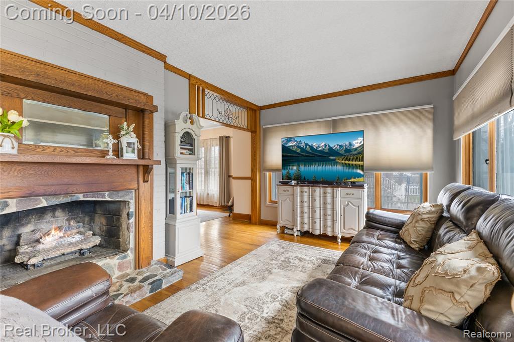 Living room with ornamental molding, a high end fireplace, and light wood-style floors
