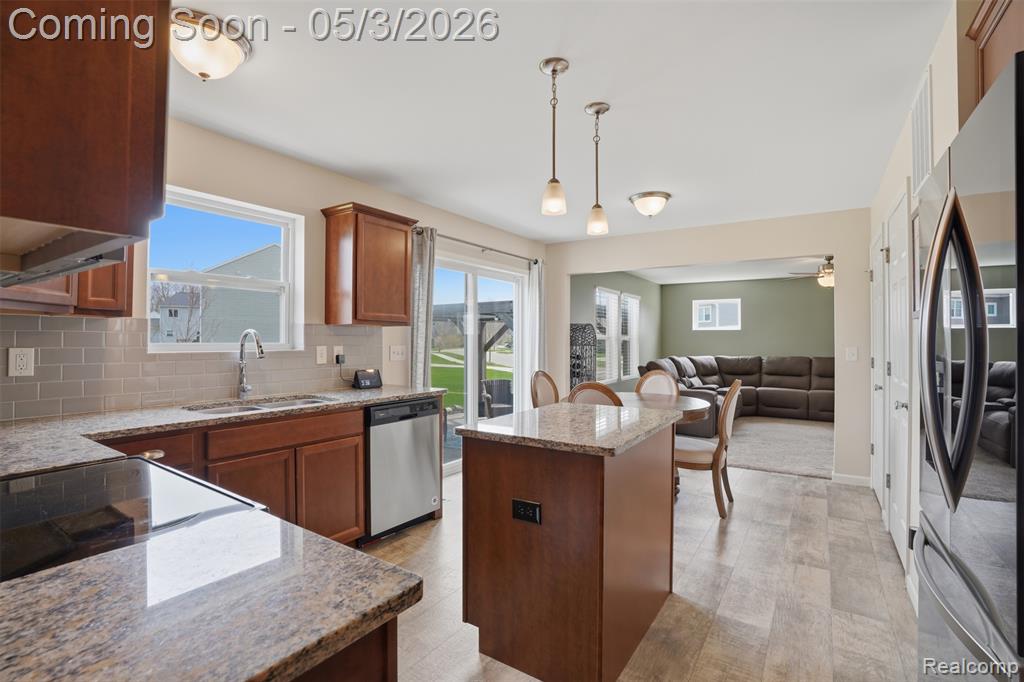 Kitchen featuring light stone counters, stainless steel appliances, open floor plan, wood finish cabinets, and tasteful backsplash